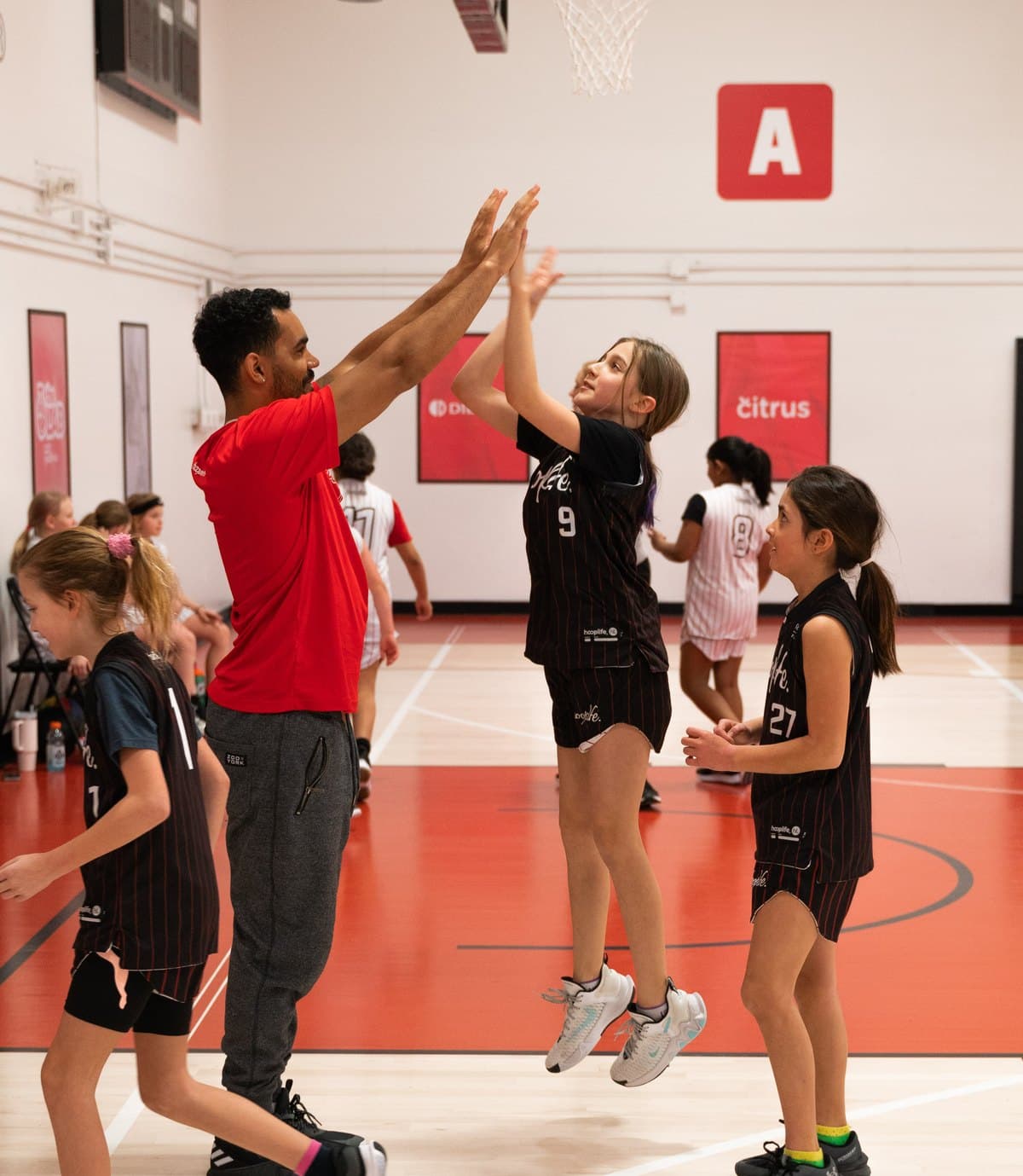 A HoopLife coach high-fiving a young player mid-game at the HoopLife Centre