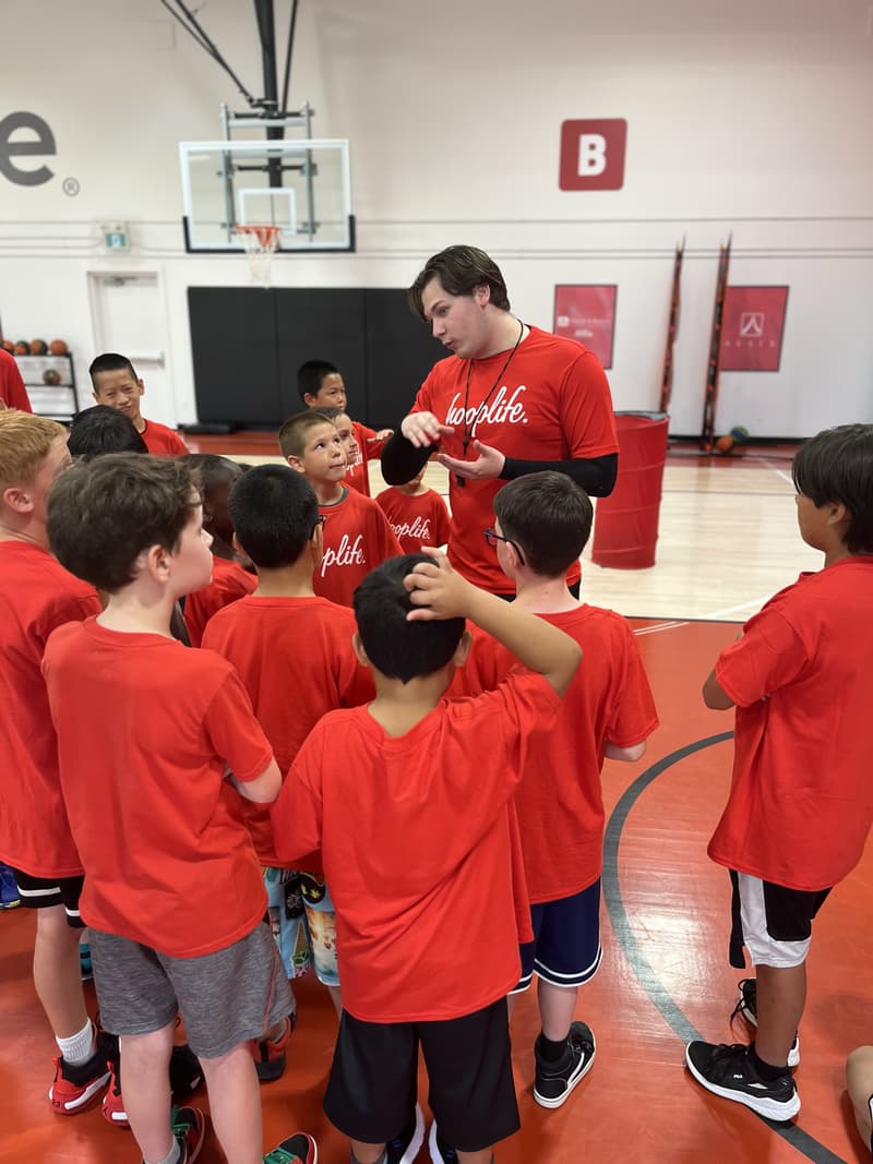 A HoopLife coach with a whistle talking to a huddle of campers