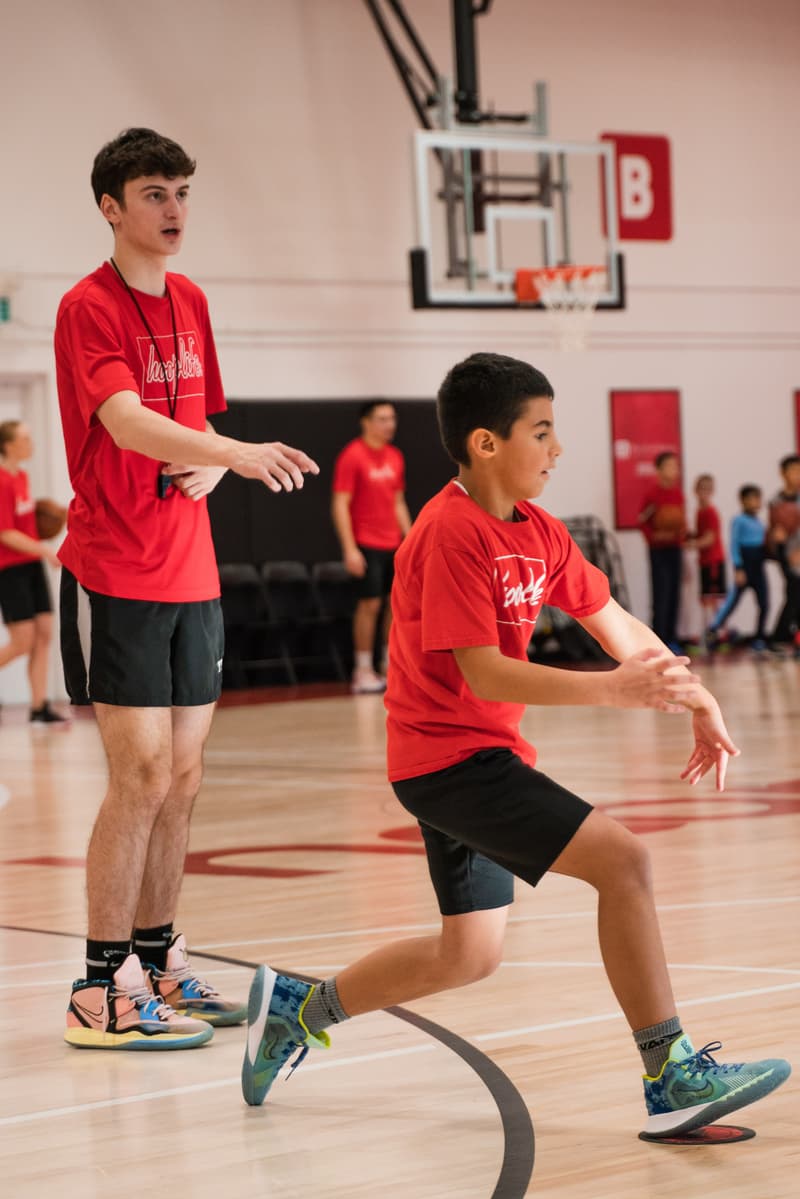 A HoopLife coach directing a camper into a defensive stance