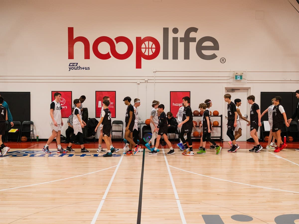 A full HoopLife gym of young players beneath the wall logo in Regina