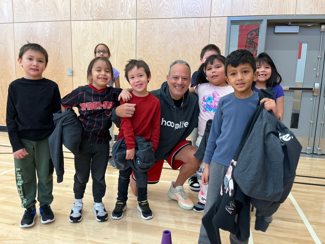 A HoopLife coach kneeling arm in arm with young players at the Iskut clinic