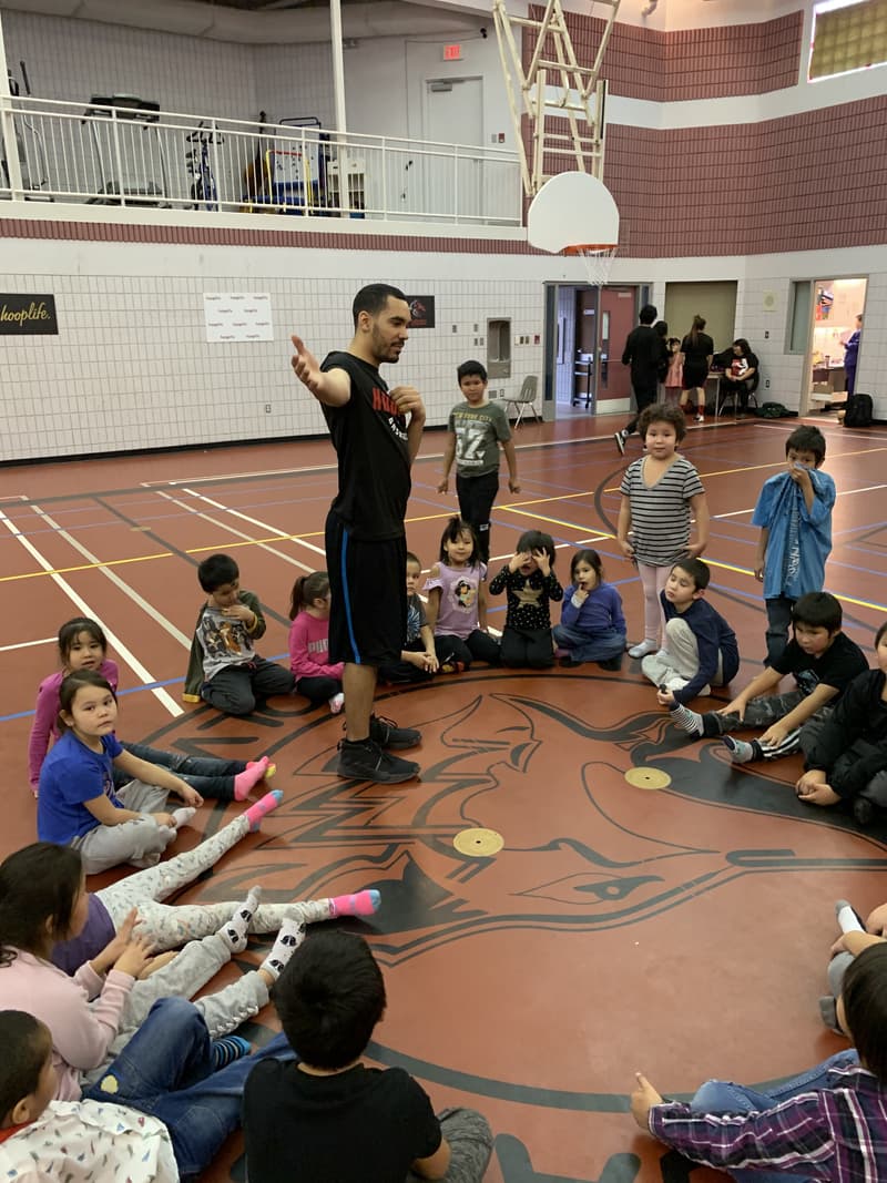 A HoopLife coach talking to a circle of young kids at centre court