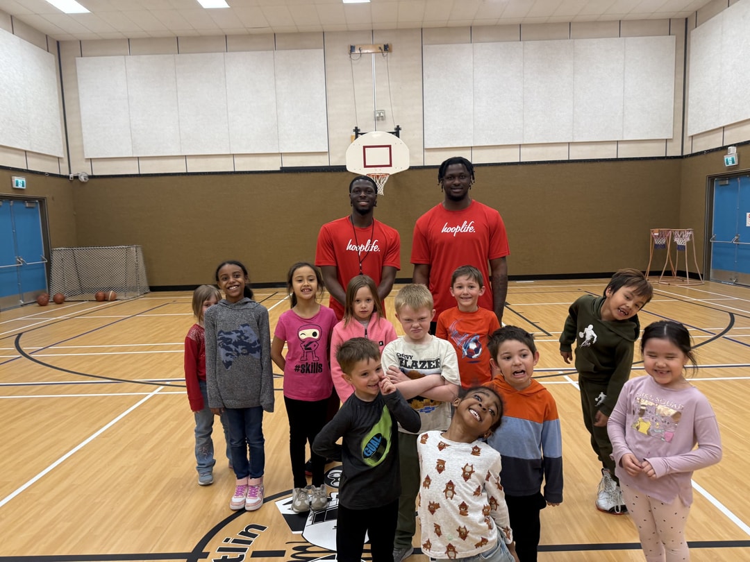 Two HoopLife coaches behind a row of laughing kids at a community clinic