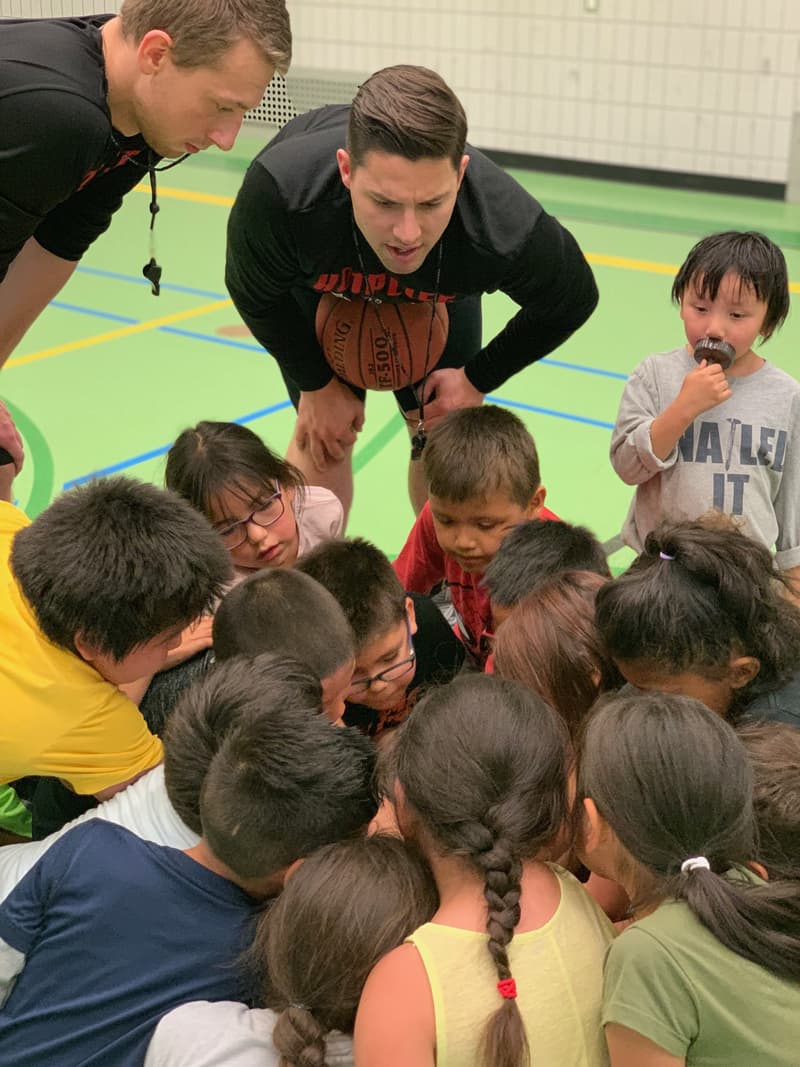 Two HoopLife coaches leaning into a huddle of young Pasqua campers