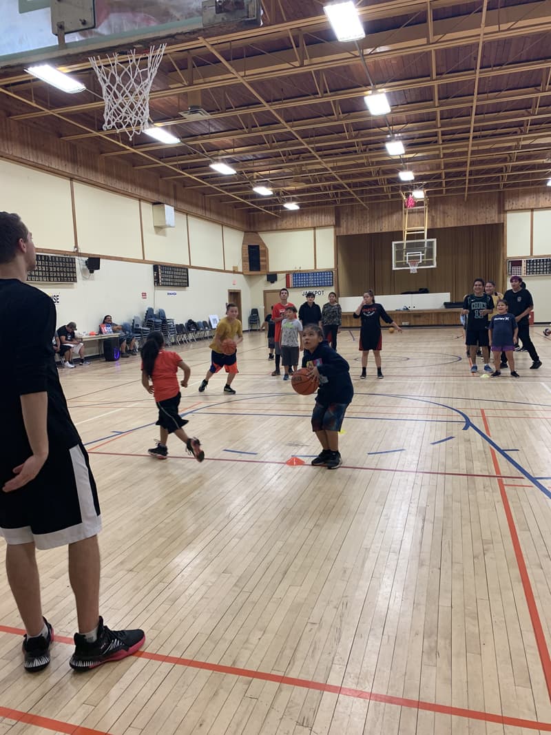 A girl lining up her shot in the Star Blanket community hall as a HoopLife coach watches