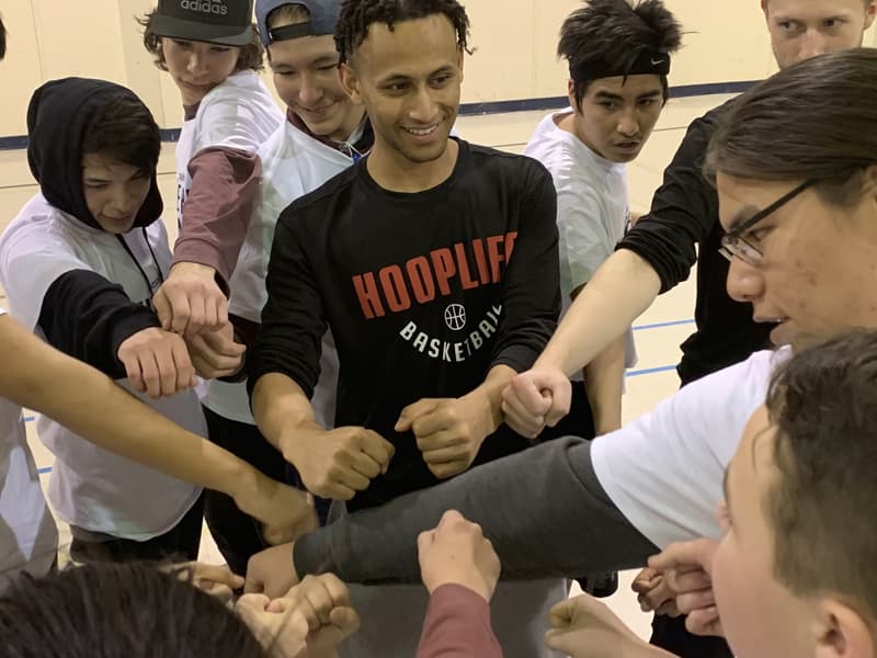 A HoopLife coach and teen campers stacking fists in the huddle