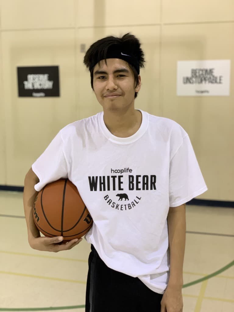 A smiling White Bear player in his White Bear Basketball shirt holding a basketball