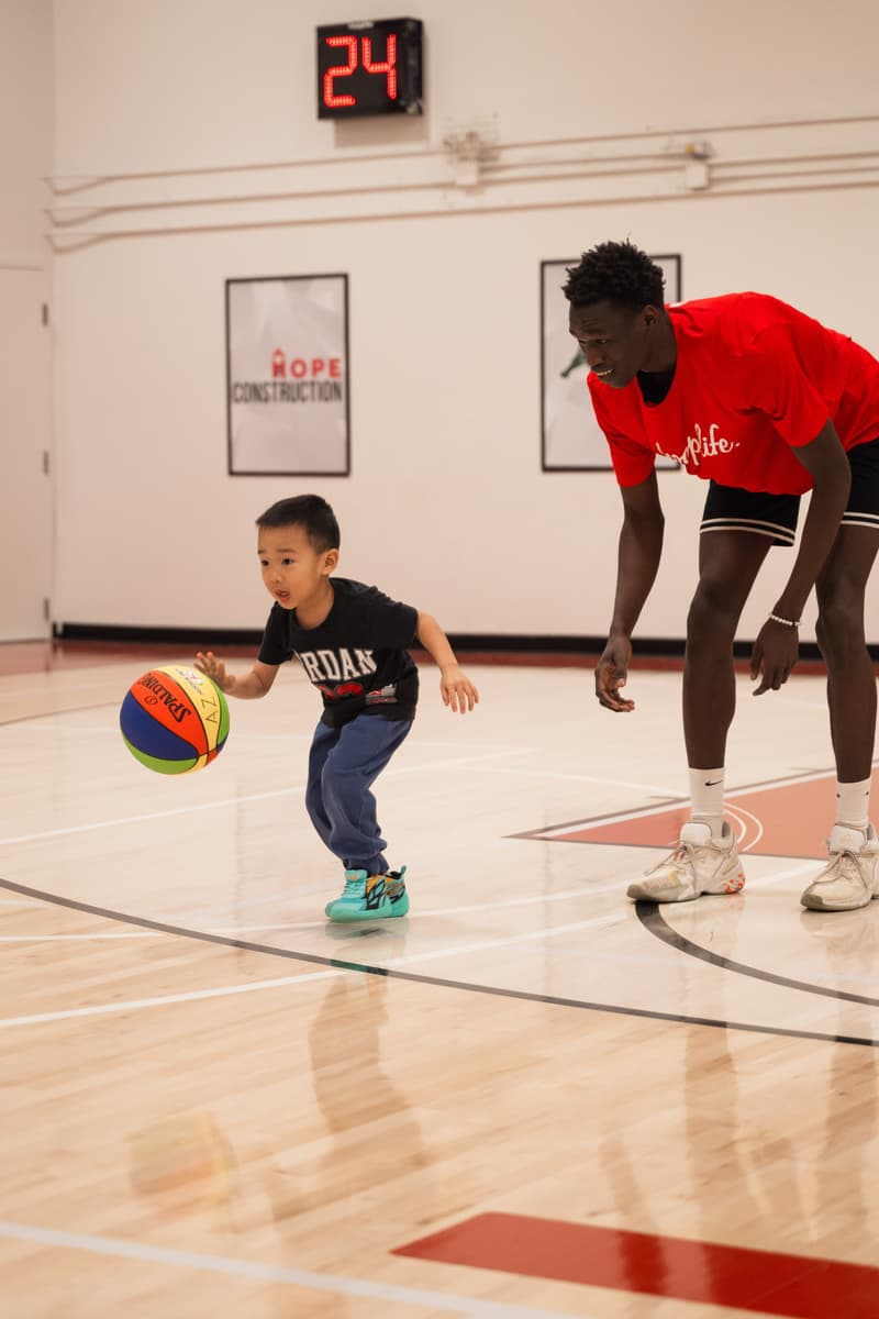 A HoopLife coach bending low to coach a Young Stars boy dribbling